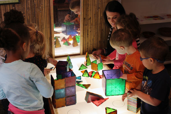 ECDC Assistant Director Joslyn Marinelli assists children building structures with colored tiles.