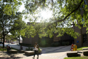 Student walking in front of French Hall with the sun peering through the trees