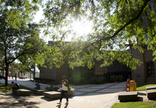 Student walking in front of French Hall with the sun peering through the trees