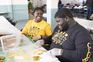 Two UM-Flint students and members of the Block Club slices pineapples during a volunteer event for More than a Day.