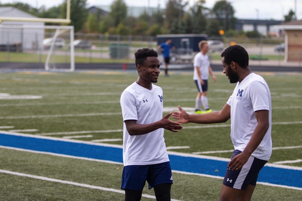 Two UM-Flint Men's Club Soccer players high five each other during practice.