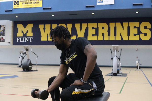A UM-Flint student lifts a weight on the gym floor of the UM-Flint Rec Center.
