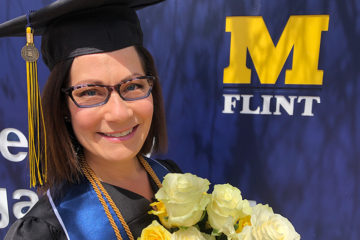 Holly Attebury in graduation regalia in front of a UM-Flint sign