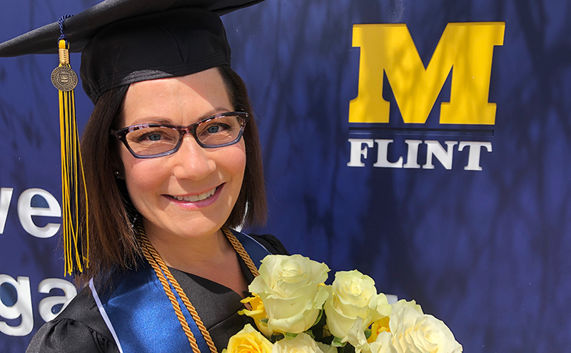 Holly Attebury in graduation regalia in front of a UM-Flint sign