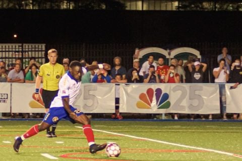 Ayuk Tambe, a UM-Flint graduate student and striker on the Flint City Bucks soccer team, goes to kick a game winning goal during a night game in August 2019.