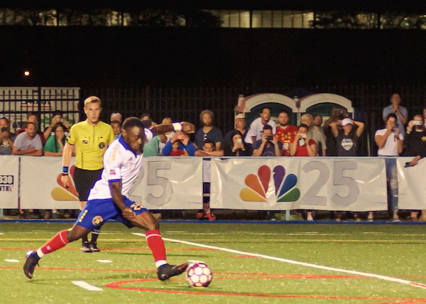 Ayuk Tambe, a UM-Flint graduate student and striker on the Flint City Bucks soccer team, goes to kick a game winning goal during a night game in August 2019.