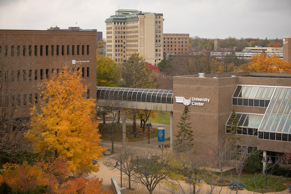 An exterior shot of campus shows the University Center with the Northbank Center in the background. The trees are orange, yellow and red in autumn.