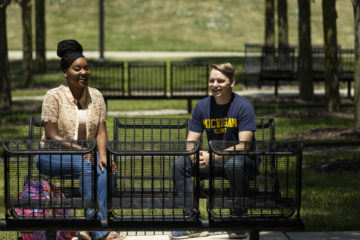 Two UM-Flint students sit and talk on a bench on campus.