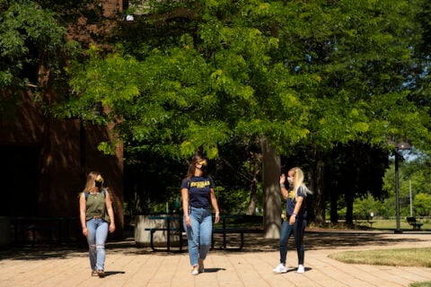 Three female students walk through the UM-Flint campus in the spring