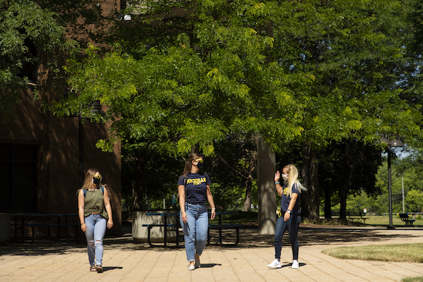 Three female students walk through the UM-Flint campus in the spring
