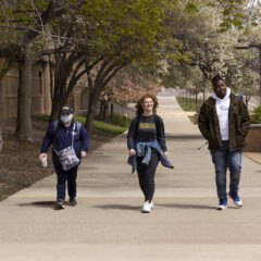 Three UM-Flint students walk along a sidewalk on campus.