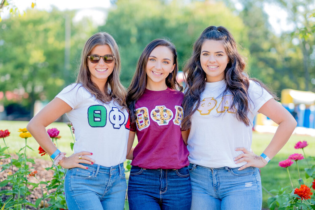 Three female students posing for the camera wearing greek letters. 