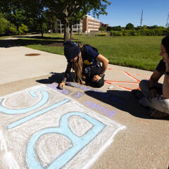 Photo of Alex Grimes drawing non-profit logo with sidewalk chalk