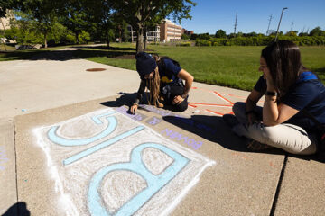 Photo of Alex Grimes drawing non-profit logo with sidewalk chalk