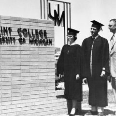 Students in graduation apparel standing next to a Flint College sign