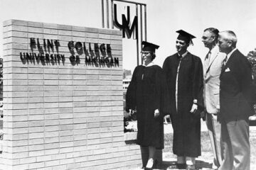 Students in graduation apparel standing next to a Flint College sign