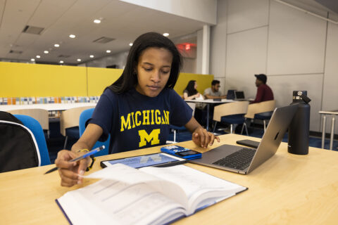 Female student studying with a book, laptop, ipad, and calculator