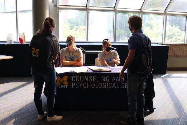 Two UM-Flint students stand at a table and talk to CAPS counselors.