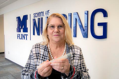 Marilyn Filter standing in front of the School of Nursing sign holding her scope invention.