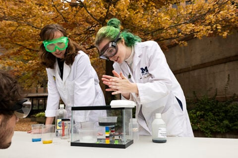 Students and professors in lab coats and goggles conducting chemistry experiments in McKinnon Plaza.