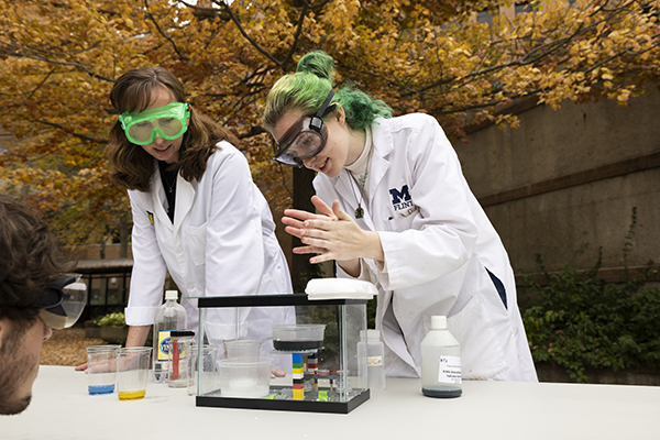 Students and professors in lab coats and goggles conducting chemistry experiments in McKinnon Plaza.