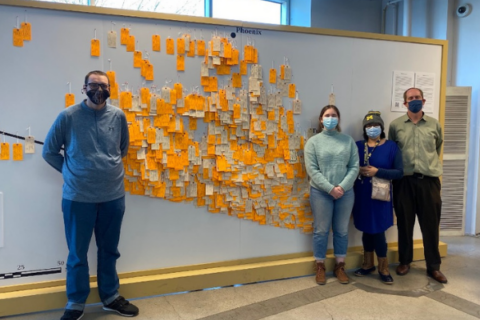4 people standing in fron of the Hostile Terrain exhibition, showing deceased migrants.