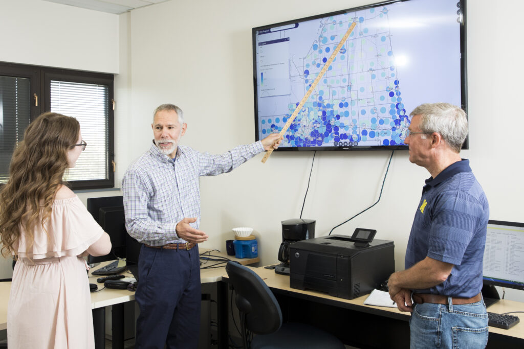 Dr. Martin Kaufman (center) explaining GIS information to two people using mapped data on a TV. 