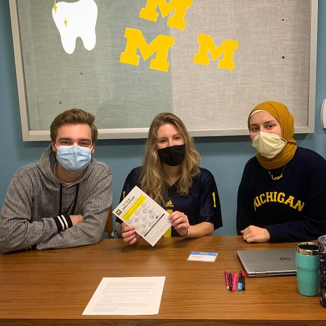 Pre-Dental Club students sit at table holding flyer 