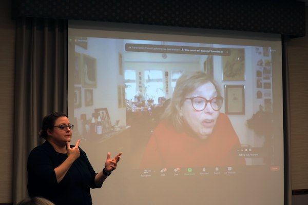 A sign language interpreter interprets Judy Heumann's comments which are broadcast live on a screen