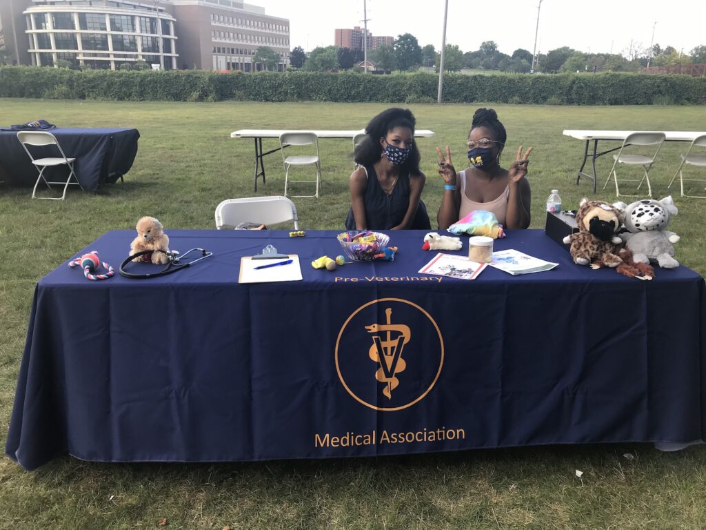 UM-Flint Pre-Vet students sitting at an informational table with stuffed animals. 