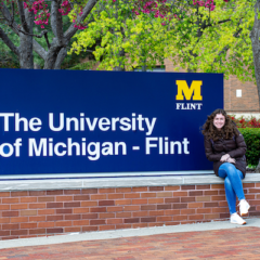 Katelyn Stuck sits by the University of Michigan-Flint sign near French Hall.