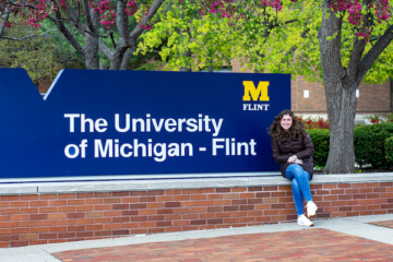 Katelyn Stuck sits by the University of Michigan-Flint sign near French Hall.
