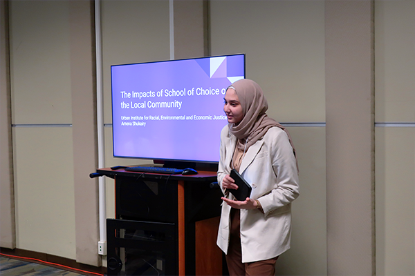 Intern Amena Header presents in front of accompanying television cart that has her presentation displayed.