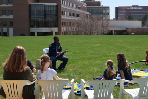 Trooper Horton reads a story to families on blankets and chairs outside of White Building on the lawn