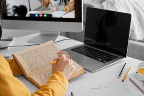 a person reading a book at a desk with a laptop.