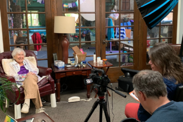 Vickie and John Larsen are set up with camera and lighting equipment to interview 105-year-old Margie Carter at home about her experiences growing up in Carriage Town in the early 20th Century