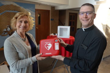 Kristi Wilson, associate professor at UM-Flint's School of Nursing presents Father Anthony of Pius X Catholic church a new, automatic defibrillator.