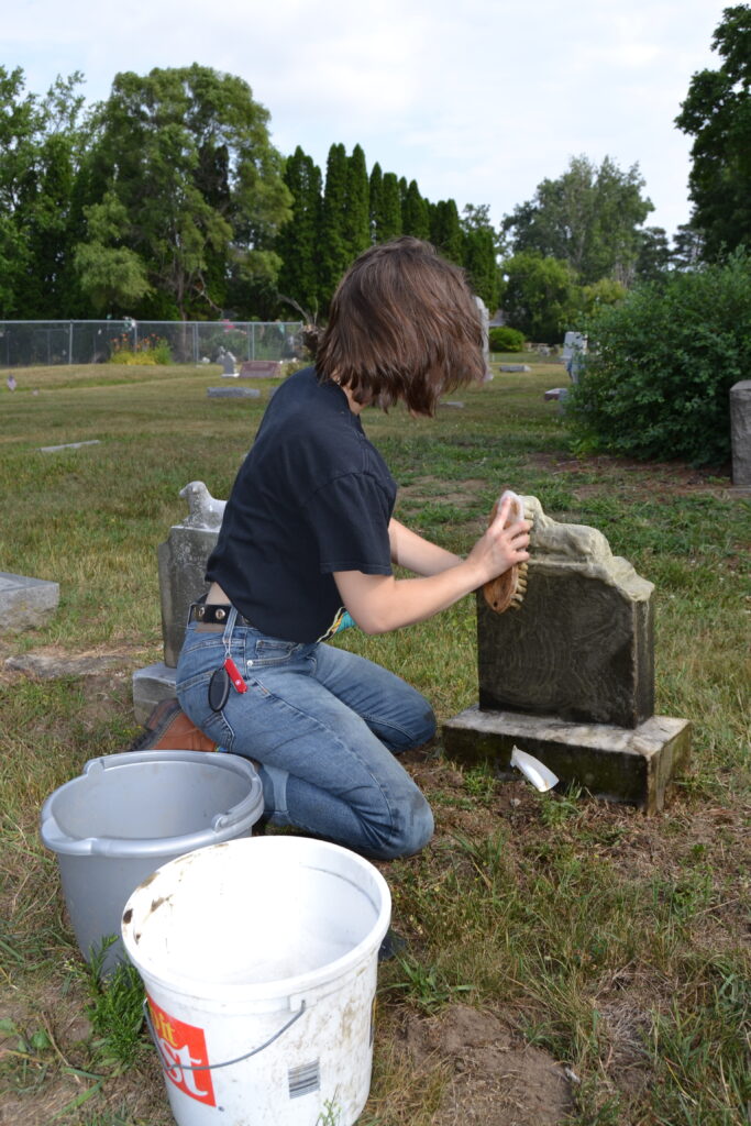 Izzy Guertin, a senior from Fenton works to carefully clean headstones at Old Calvary Catholic Church. (Photo Credit: Madeline Campbell)