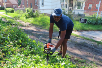 UM-Dearborn student Jacques Jones cuts down small trees and trims overgrown brush in the alley way.