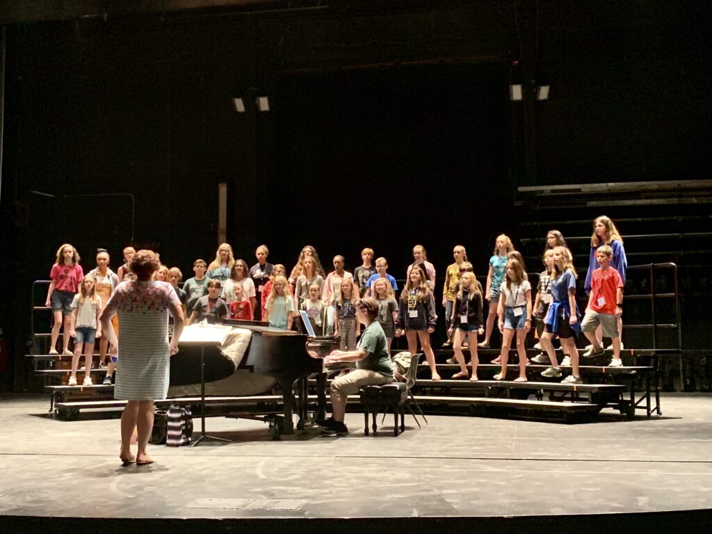 Attendees standing on risers with piano accompaniment. 