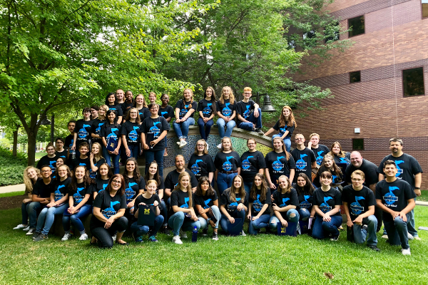 attendees of the summer vocal music academy pose for a group photo. The campers are all wearing camp t shirts.