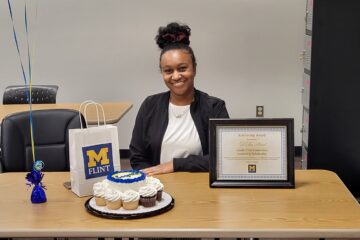 D'Asia Beard sitting a desk with UM-Flint cupcakes and plaque