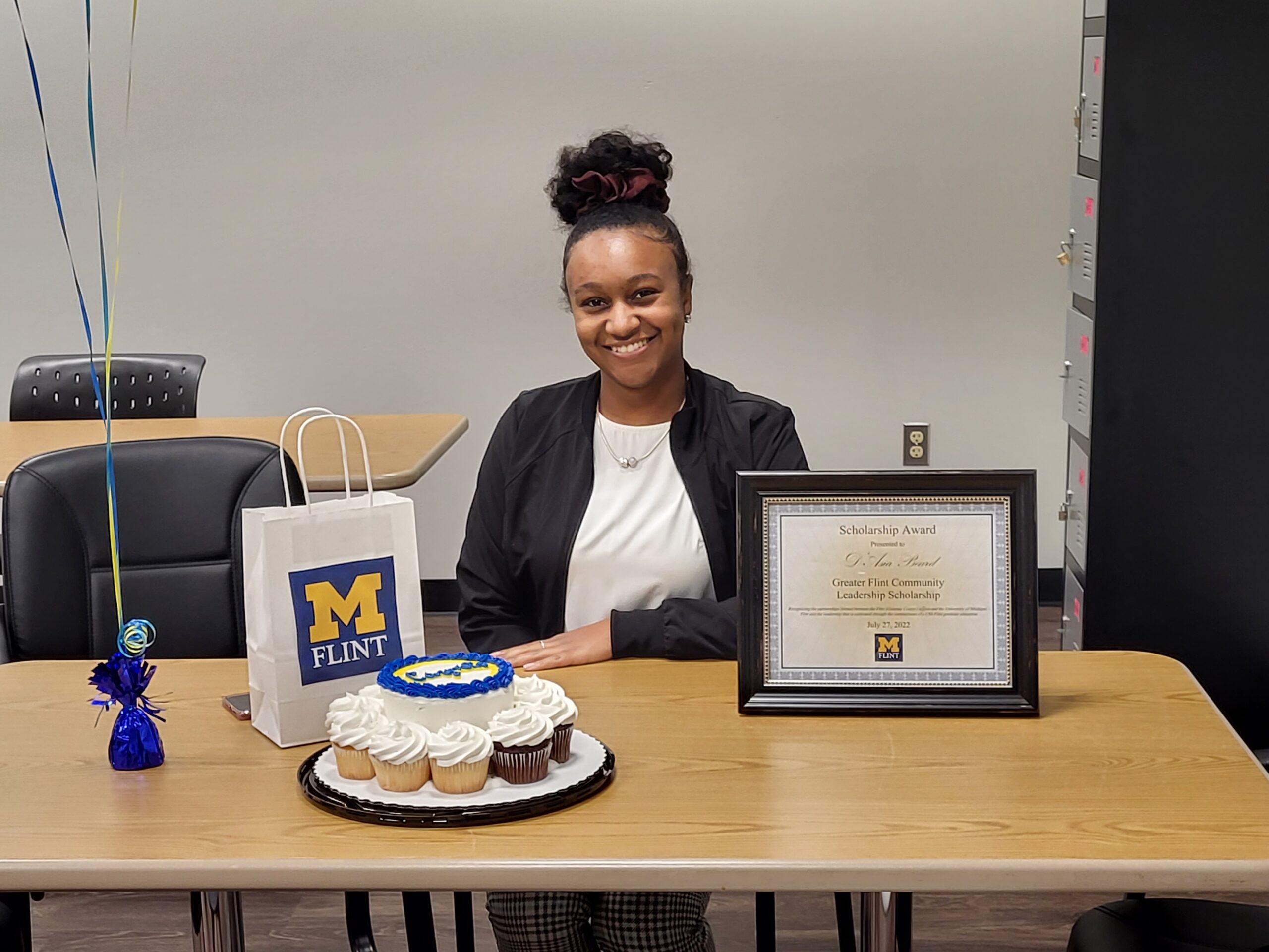 D'Asia Beard sitting a desk with UM-Flint cupcakes and plaque