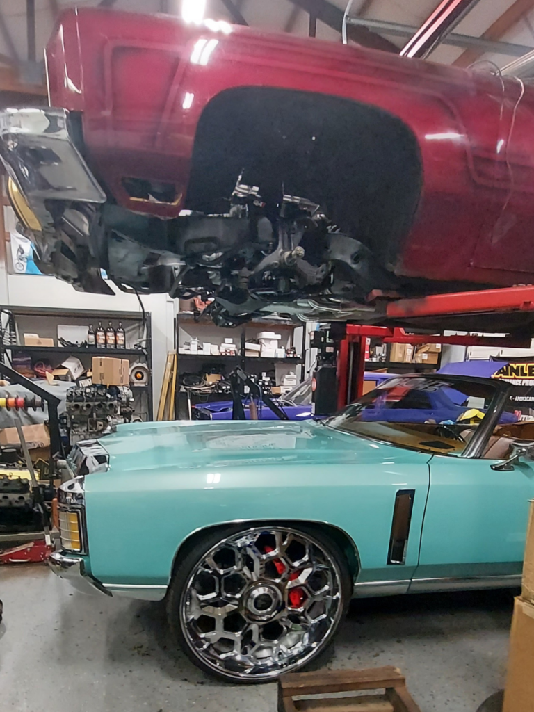 Raised up red Donk in the shop with a blue one parked underneath.