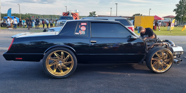 Black Donk with Gold rims gets trackside adjustments on its open chassis engine.