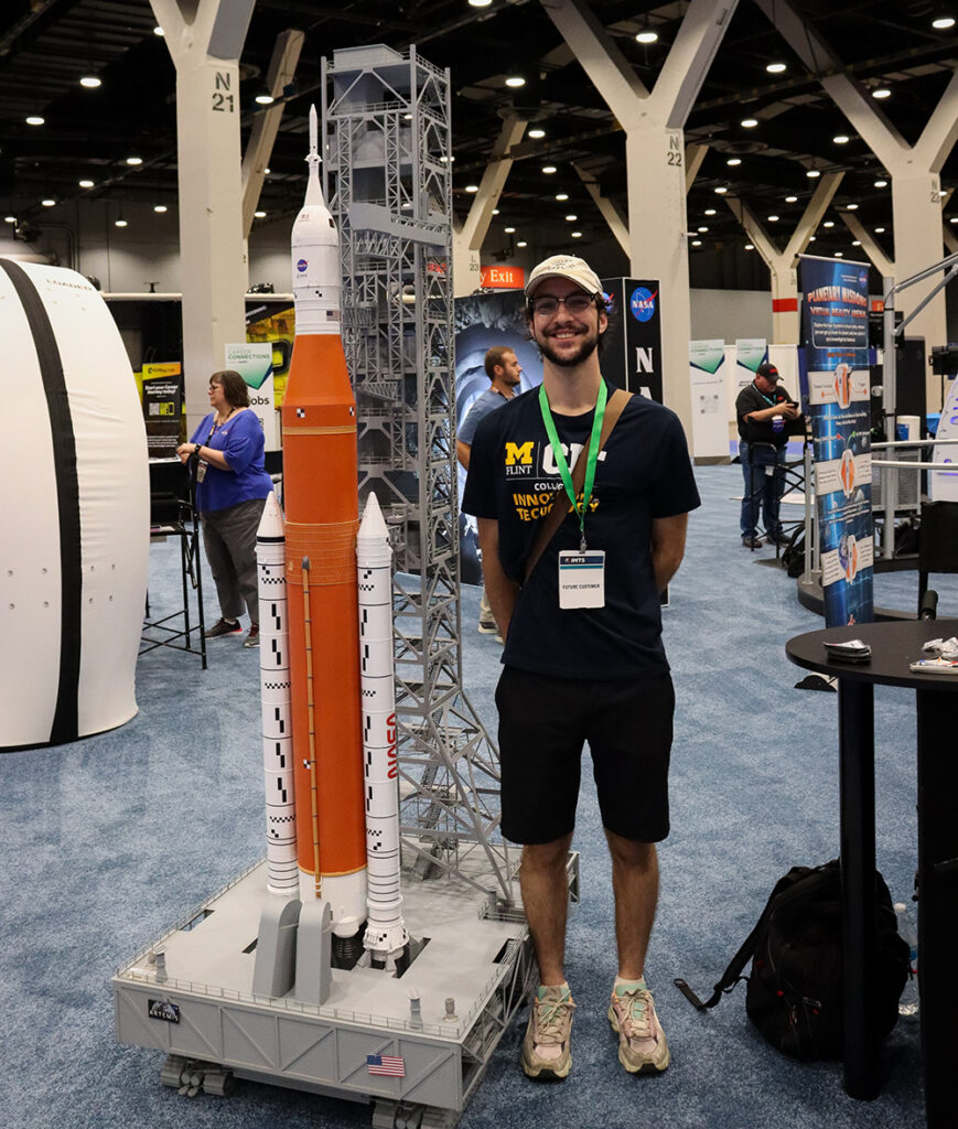 Zach Smith posing next to a scale model of a NASA rocket. 