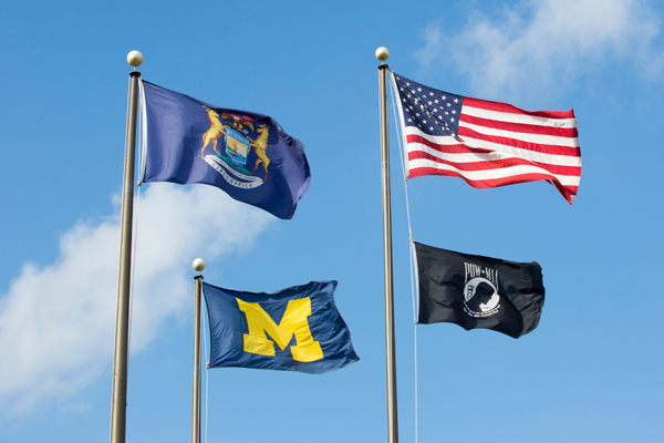 Four flags against a blue sky: the US flag, the Michigan flag, the POW MIA flag and the U-M flag