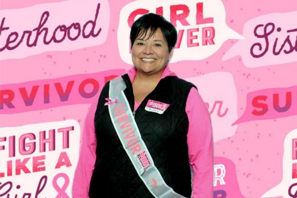 Micaela Trevino posing in front of a pink breast cancer surivivor banner