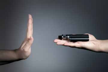 A person holding their hand up to say "no" to another hand holding a vaping device.