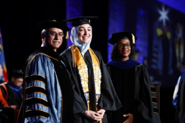 A student on stage receiving her diploma with Chancellor Deba Dutta and Provost Sonja Feist Price